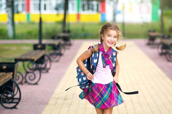 Cheerful girl with a backpack and in a school uniform in the school yard. Cheerful girl with a backpack and in a school uniform in the school yard.